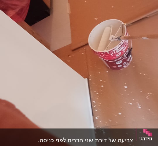 דלי צבע ורולר על רצפה מוגנת במהלך עבודת צביעת קיר
